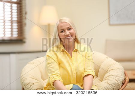 Portrait Of Happy Mature Woman Sitting In Papasan Chair At Home