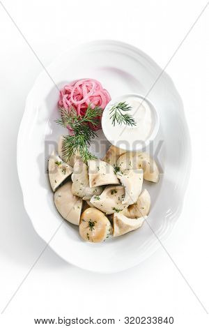 Pickles set with homemade pickled milk mushrooms, marinated red onion rings and sour cream on white restaurant plate isolated. Salted Lactarius resimus mushroom with oil and fresh chopped dill