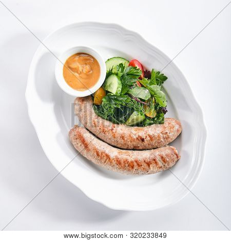 Top view of Munich sausages for frying made from pork and beef with mustard sauce and mixed salad isolated. Traditional German rostbratwurst, wurst or bratwurst with vegetables and greens topview