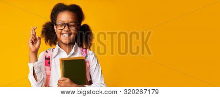 African American Elementary School Girl Keeping Fingers Crossed For Luck In Studio, Yellow Backgroun
