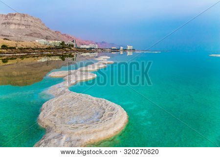 Azure sea water is full of healing salts. Small islets and path of salt in the water. Early morning at the resorts of the Dead Sea. Israel. Concept of ecological, medical and photo tourism