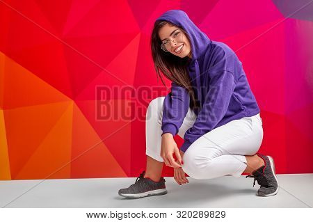 Cool Modern Woman In Street Wear Hunkering Over Bright Colourful Background Smiling At Camera