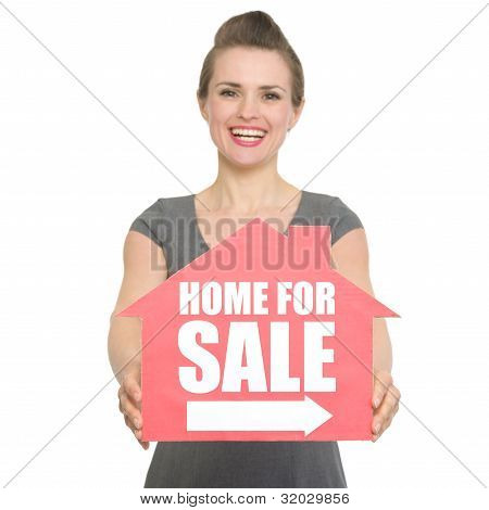 Portrait Of Smiling Realtor Showing Home For Sale Sign Isolated
