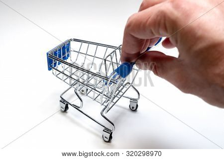 A Male Hand Is Rolling A Souvenir Shopping Trolley On A White Background. Online Shopping Concept. C