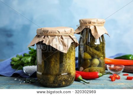 Jars With Pickled Cucumbers On Wooden Table Against Blue Background
