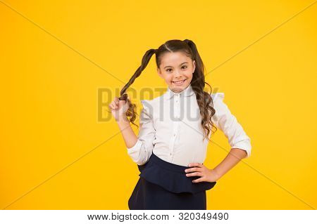 Her Twisted Hairdo. Small Girl Winding Long Hairdoaround Her Finger On Yellow Background. Little Kid