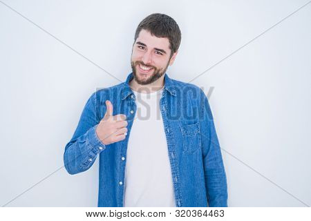 Young handsome hispanic man wearing denim jacket over white isolated background doing happy thumbs up gesture with hand. Approving expression looking at the camera with showing success.