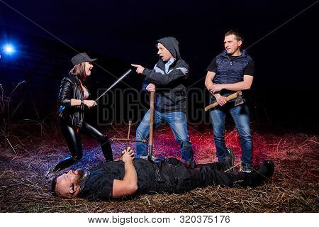 Three Bandits Near Dead Man In The Field At Night. Photoshoot About Life Of Gungsters In Russia