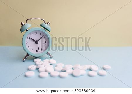 Pills Lie Next To The Alarm Clock On A Light Background. Healthcare And Medicine Concept.