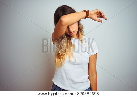 Young beautiful woman wearing casual white t-shirt over isolated background covering eyes with arm, looking serious and sad. Sightless, hiding and rejection concept