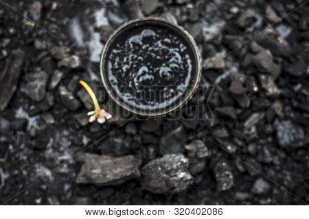Close Up Of Activated Charcoal In A Glass Bowl On The Wooden Surface Along With Some Raw Powder Of C