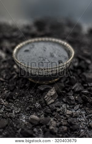 Close up of activated charcoal in a glass bowl on the wooden surface along with some raw powder of c