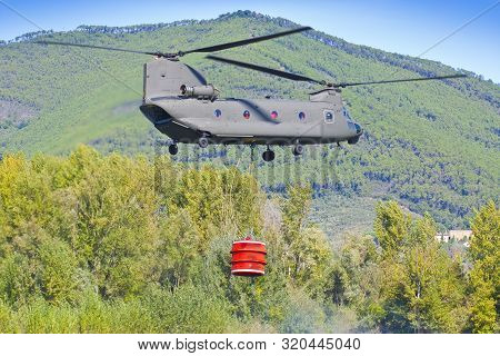 Firefighting Helicopter Of The Italian Army Is Carrying A Metal Bucket Full Of Water To Extinguish A
