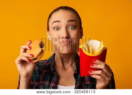 Hungry Girl Eating Burger And French-fries On Yellow Background. Cheat Meal And Junk Food. Studio Sh
