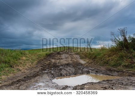 Dirt Road After Heavy Rain Leading To The Top Of The Hill, Stormclouds On The Dark Sky.