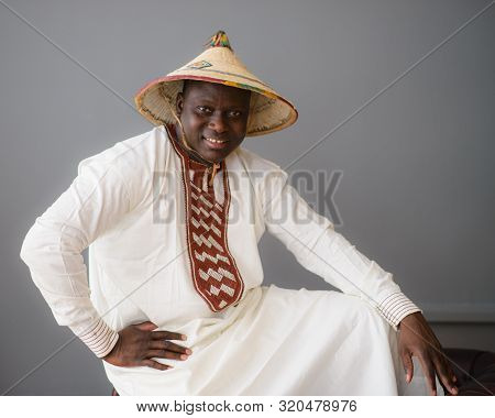 Handsome African Man In Traditional White Dress And Fulani Hat On Gray Background