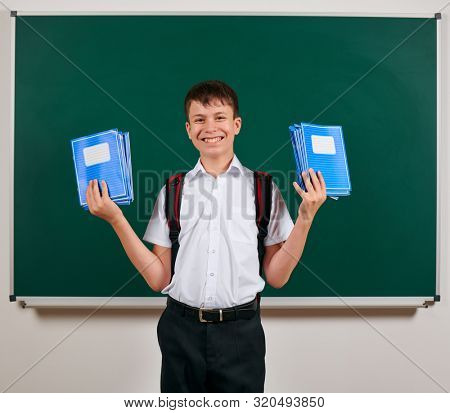 Portrait of a school boy posing with backpack and school supplies, blackboard background - back to school and education concept