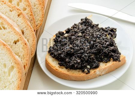 Tapenade Sandwich On A Sauser And Sliced Wheat Bread On A Wooden Chopping Board Over White Kitchen T