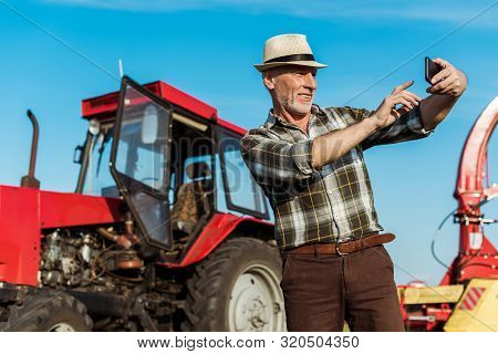 Selective Focus Of Happy Self-employed Farmer Taking Selfie Near Tractor