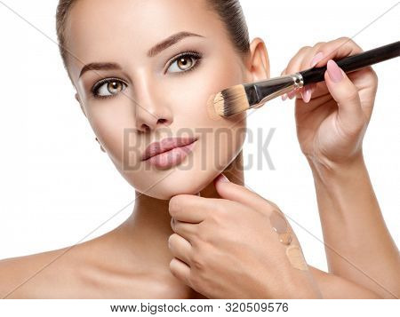 Makeup artist applying liquid tonal foundation  on the face of the woman