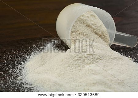 Overturned Measuring Scoop With Protein Powder On Wooden Table, Closeup