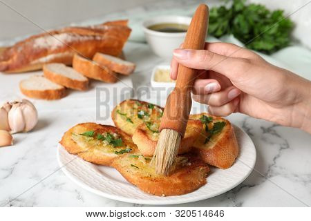 Woman Brushing Slices Of Delicious Toasted Bread With Garlic And Herbs On White Marble Table, Closeu