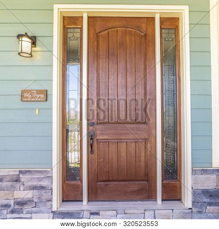 Square Frame Front View Of A Home With Green Wall And Brown Wood Door Flanked By Sidelights