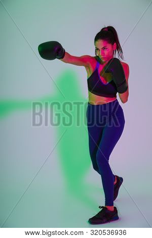 Photo of young beautiful fitness woman boxer isolated with led flash lights make boxing exercises in gloves.
