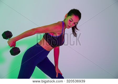 Image of beautiful young fitness woman isolated with led flash lights make exercises with dumbbells for arms triceps.
