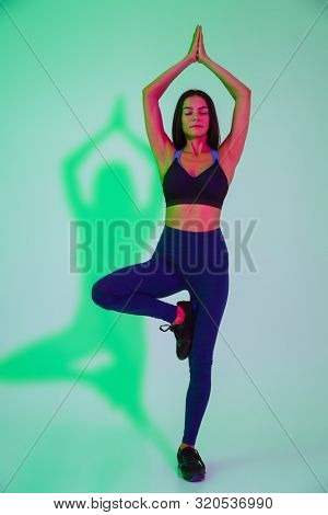 Image of concentrated young strong fitness woman posing isolated with led flash lights make yoga exercises.