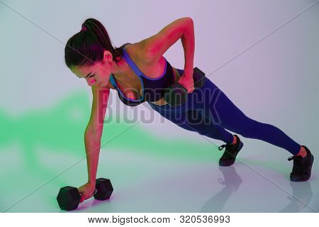 Photo of amazing attractive young fitness woman isolated with led flash lights make exercises with dumbbells for arms.