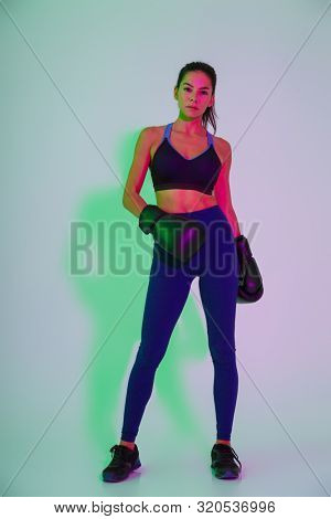 Image of young serious beautiful fitness woman boxer posing isolated with led flash lights in gloves.