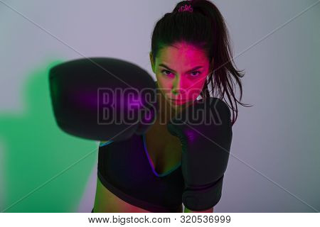 Photo of young beautiful fitness woman boxer isolated with led flash lights make boxing exercises in gloves.