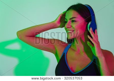 Image of cheerful optimistic young strong fitness woman isolated with led flash lights listening music with headphones.
