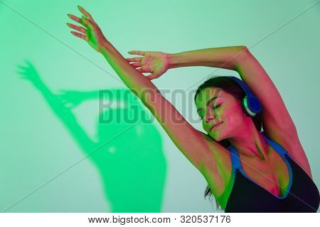 Photo of positive young strong fitness woman make stretching exercise isolated with led flash lights listening music with headphones.