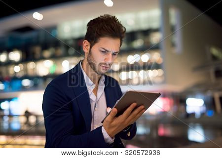 Portrait of young business man using his tablet in a city at night