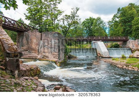 Wooden Bridge Over The River Vilia In Vilnius With A Waterfall In The Park Belmonto.