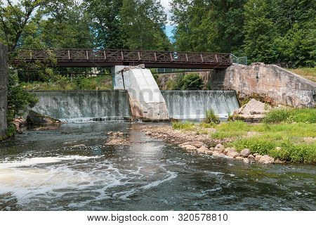 Wooden Bridge Over The River Vilia In Vilnius With A Waterfall In The Park Belmonto.