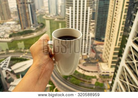 Female Hand Holds Big White Cup Of Morning Coffee With City Skyscrapers View Of Modern City Dubai. C