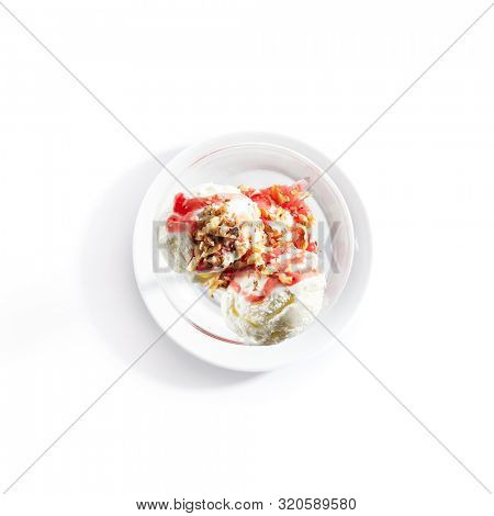 Top view of two ice cream balls or iced cream with strawberry sauce and nuts on white restaurant plate isolated. Frozen creamy yogurt ball with fruit syrup and walnuts topping topview