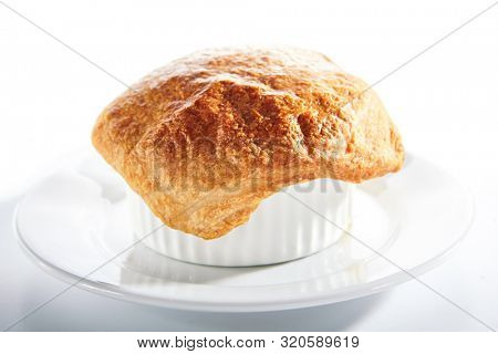 Macro shot of julienne or potage soup with chicken and mushrooms topped with melted cheese or puff pastry on white restaurant plate isolated. Stew baked in white bowl with bread on top closeup