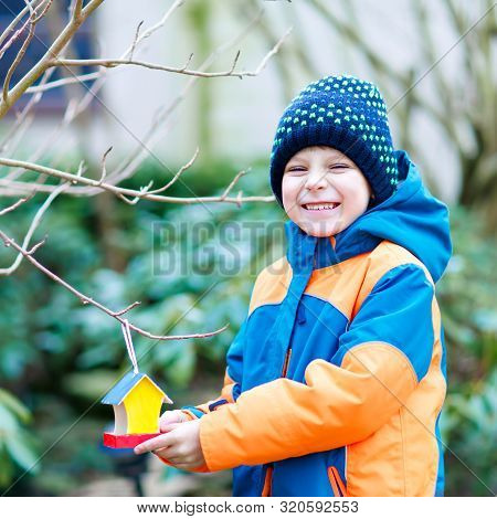 Little Kid Boy Feeding Birds In Winter. Cute Happy Preschool Child Hanging Colorful Selfmade Bird Ho