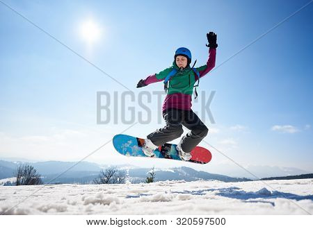 Young Female Snowboarder Jumping In Air On Copy Space Background Of Clear Bright Blue Sky And Snowy 