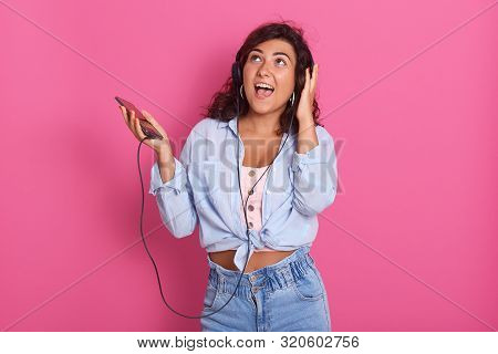 Beautiful And Happy Young Woman Listen To Music With Headphones, Isolated Over Pink Stuio Background