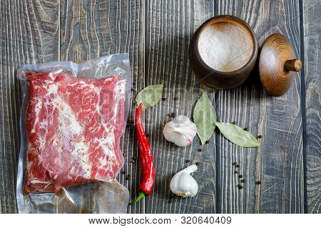 The Meat Is Packed In A Vacuum With Spices And Pepper And A Nitrite Salt On Wooden Background.