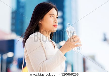 lifestyle and people concept - young asian woman drinking water flom plastic bottle in city