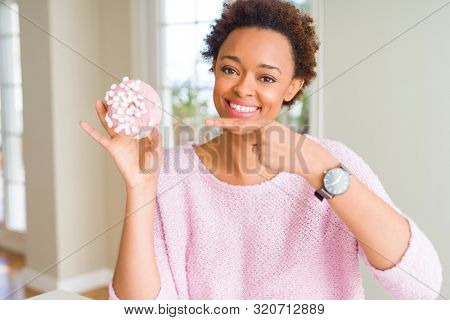 Young african american woman eating pink sugar marshmallows donut very happy pointing with hand and finger