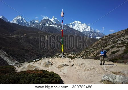 Tourist is standing next to buddhist praying flags on the Everest trek in Himalayas mountains, Near Pheriche pass. Sagarmatha national park, Solukhumbu, Nepal