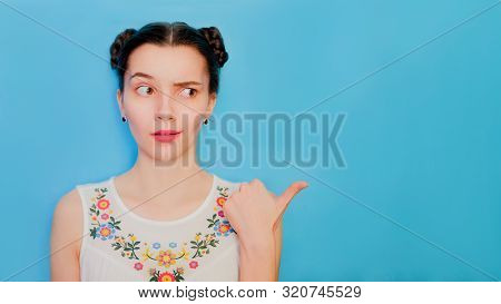 Funny Cute Girl On A Blue Studio Background. Bright Emotional Female Portrait. Woman Raises One Eyeb
