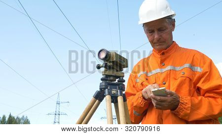 Surveyor Types On Smartphone And Looks Through Theodolite